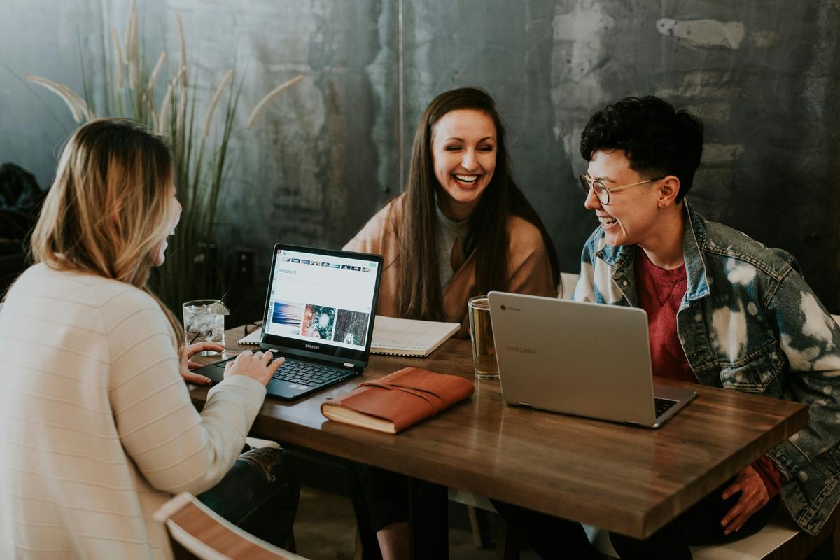 Three people are sitting at a wooden table, using laptops and debating the difference between Microsoft Office and Office 365.