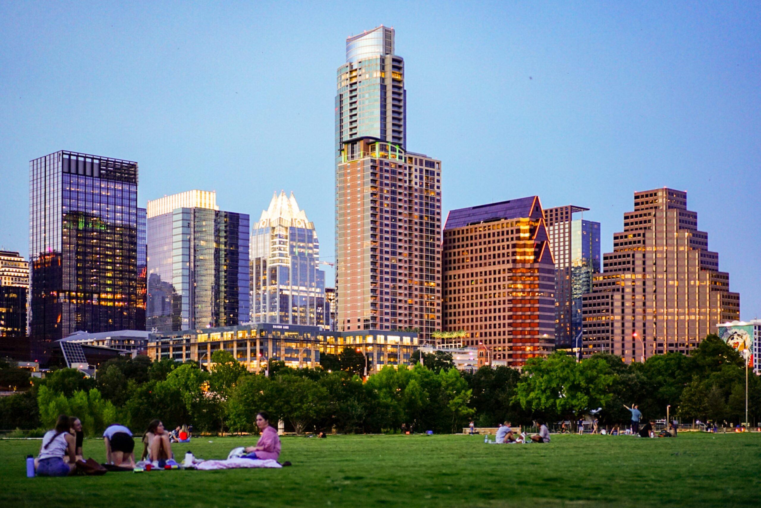 A group of people sitting on a grassy field in front of the Austin skyline, full of businesses relying on outsourced IT services.