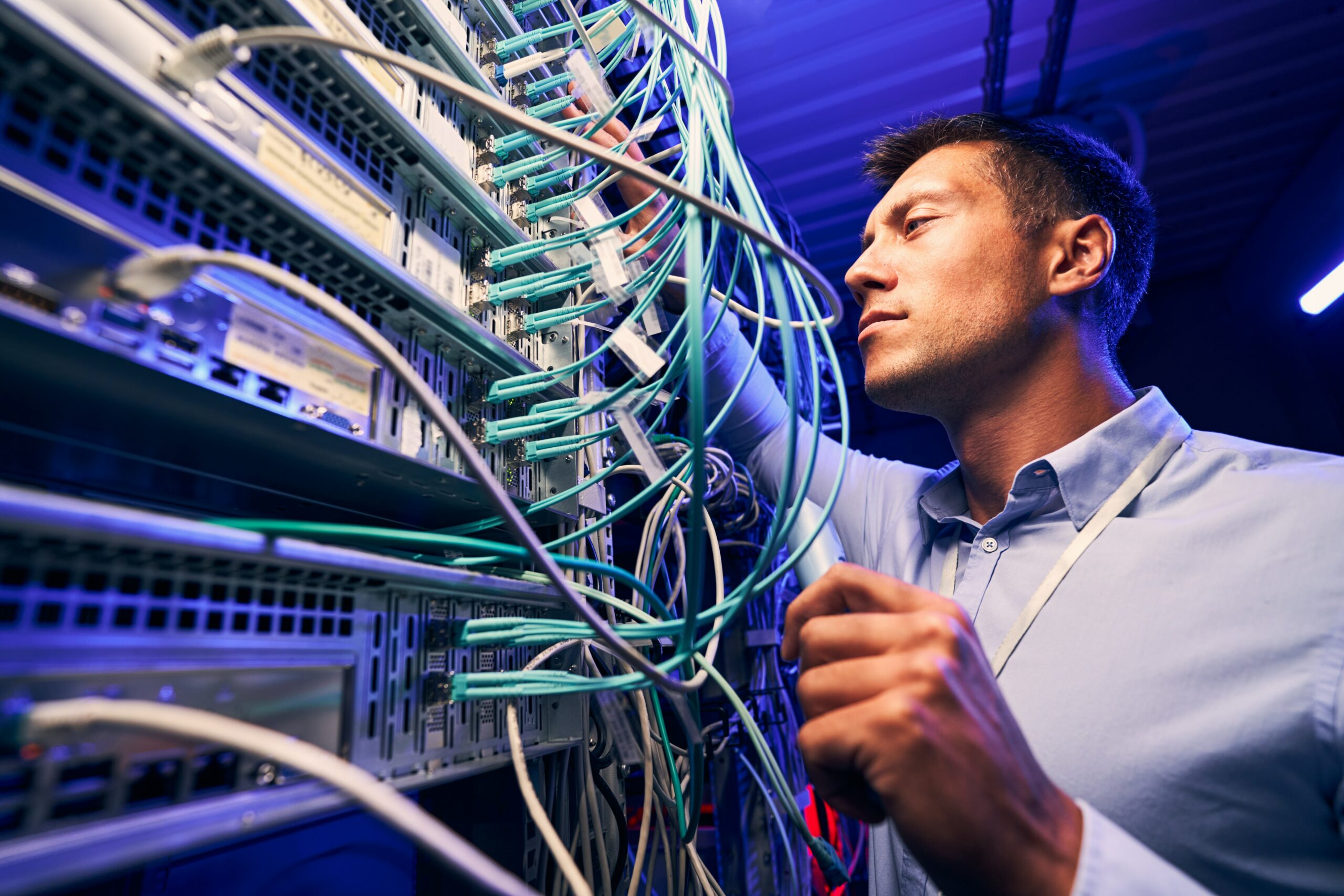 A man is working on a server in a data center, assessing security threats.