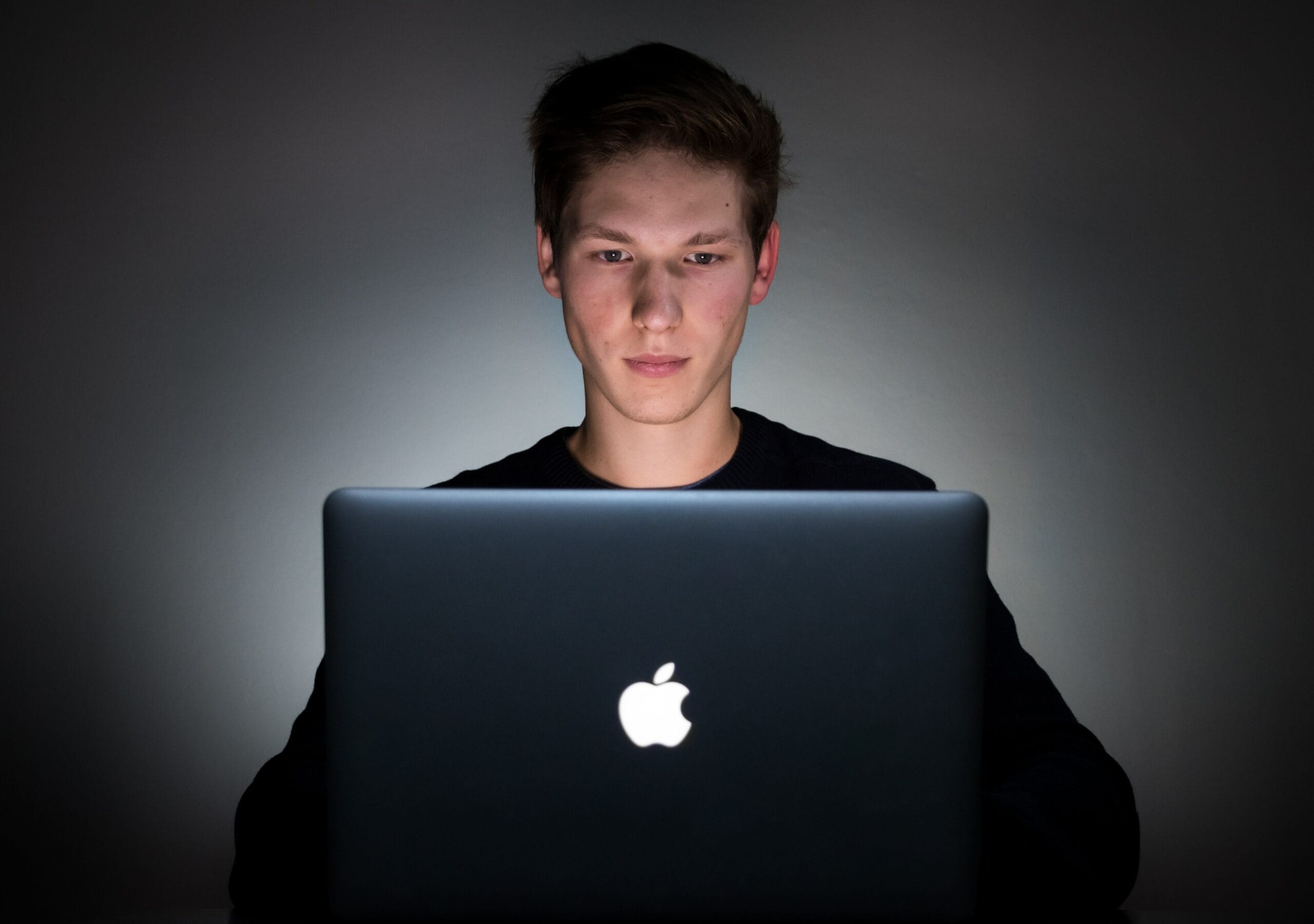 A young man assumes virtual CISO responsibilities with an apple laptop in front of a dark background.