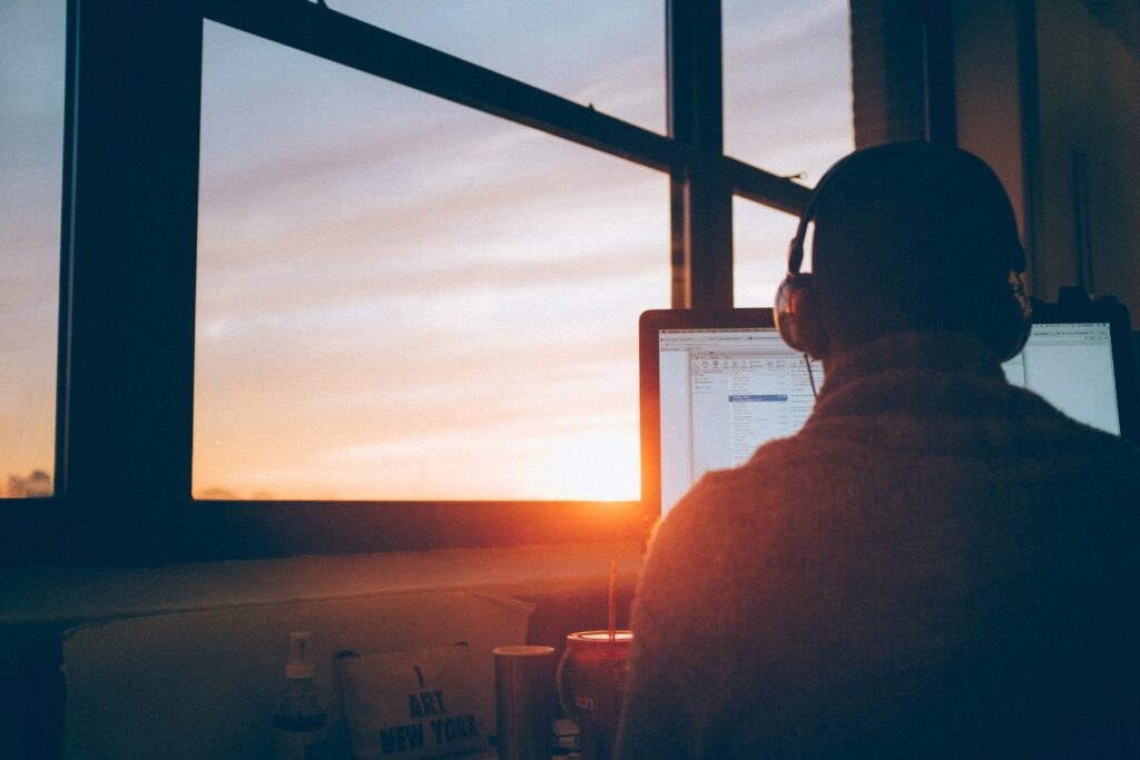 A person working on a computer in front of a window at sunset, providing DevOps as a Service.