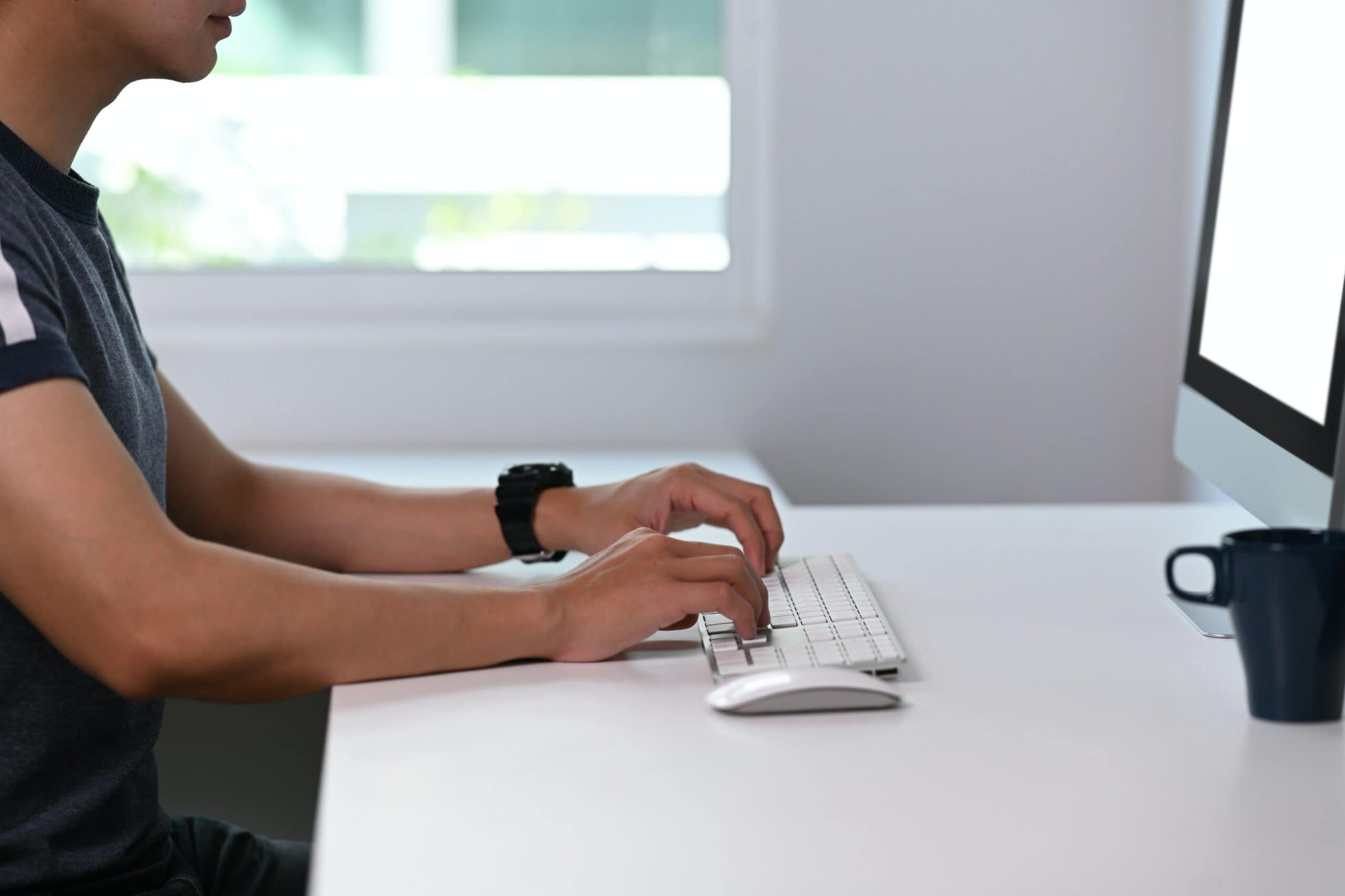 A man is sitting at a desk and typing on a computer, teleworking from home once he established how should you secure your home wireless network for teleworking.