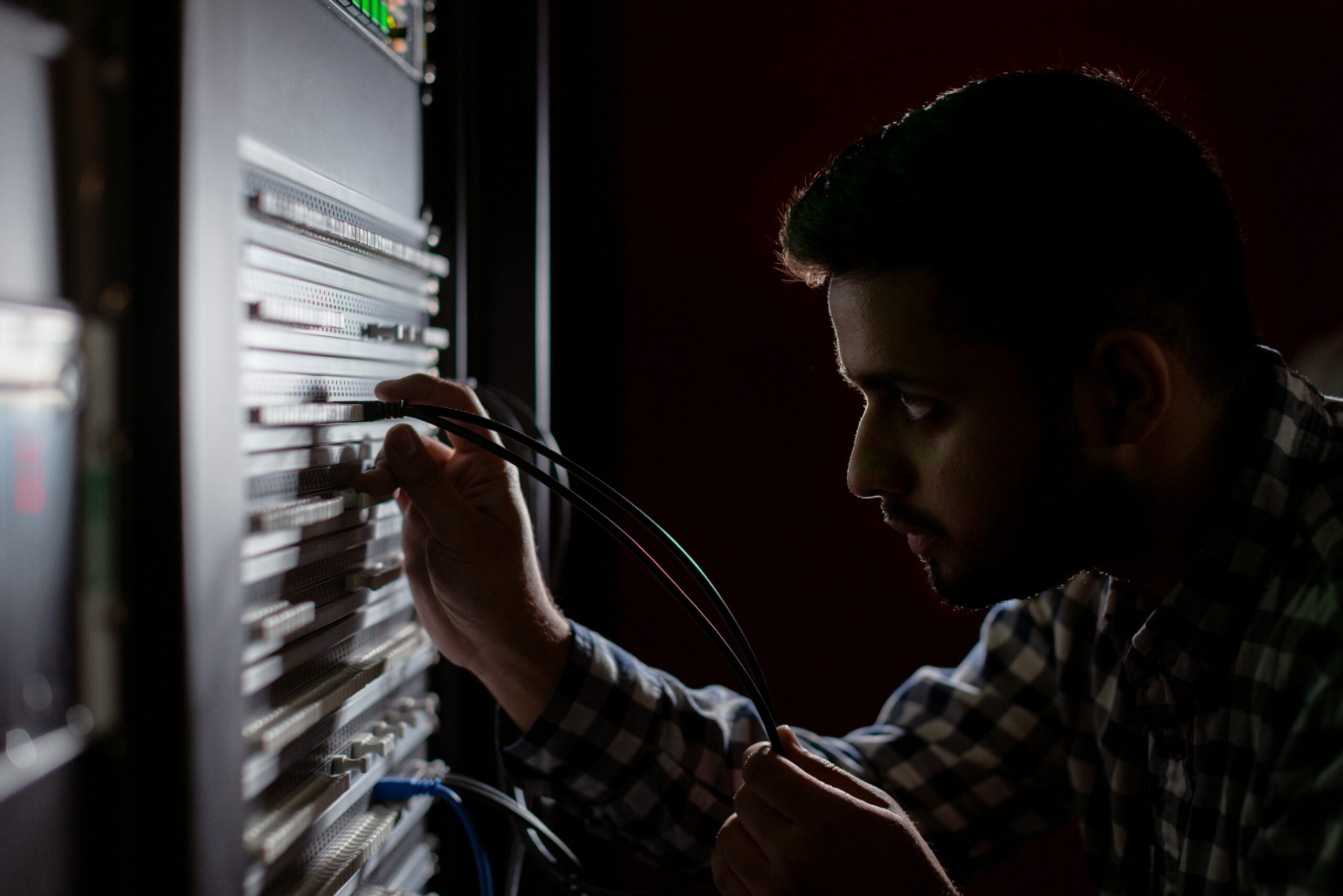A man is working on a server in a dark room, optimizing network infrastructure.