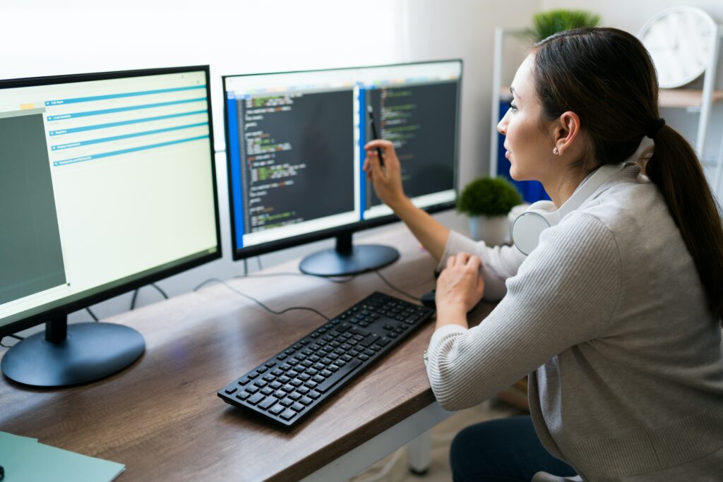 A woman working on a computer with two monitors, researching providers of IT consulting and services.