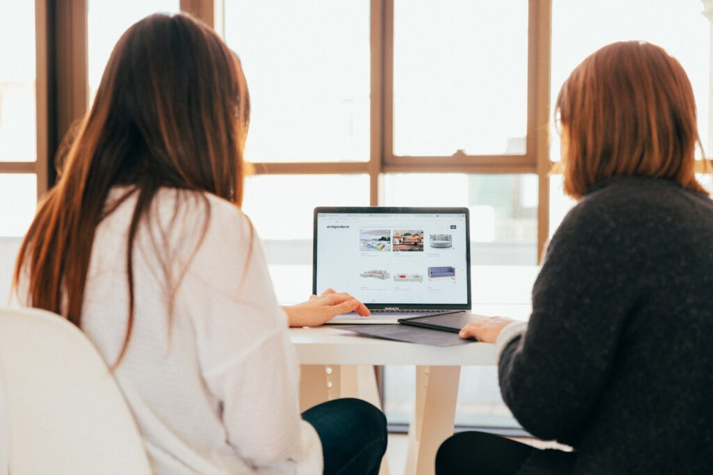 Two women sitting at a table conducting cloud security assessments using a laptop.