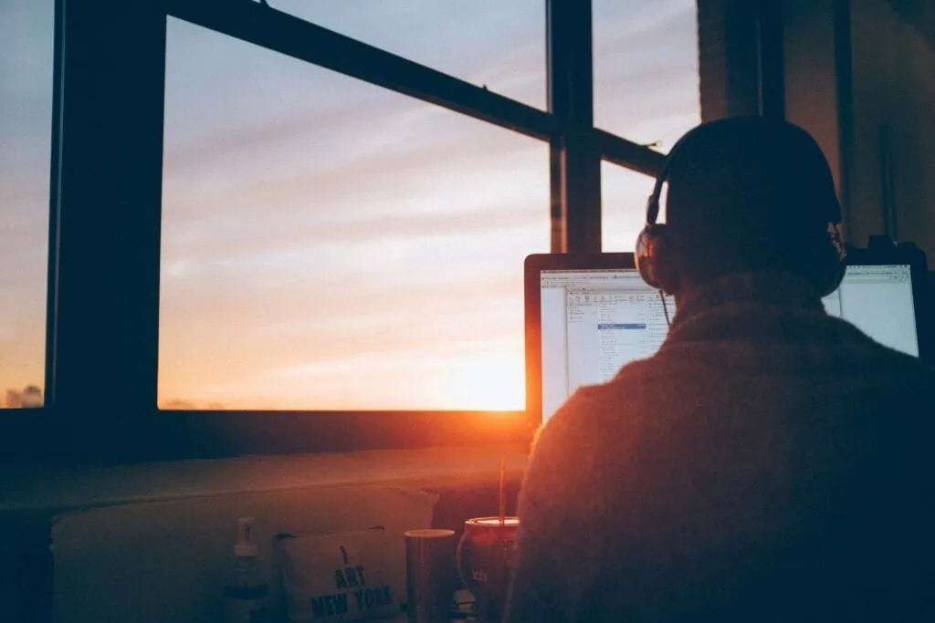 A person providing IT consulting services, diligently working on a computer in front of a window at sunset.