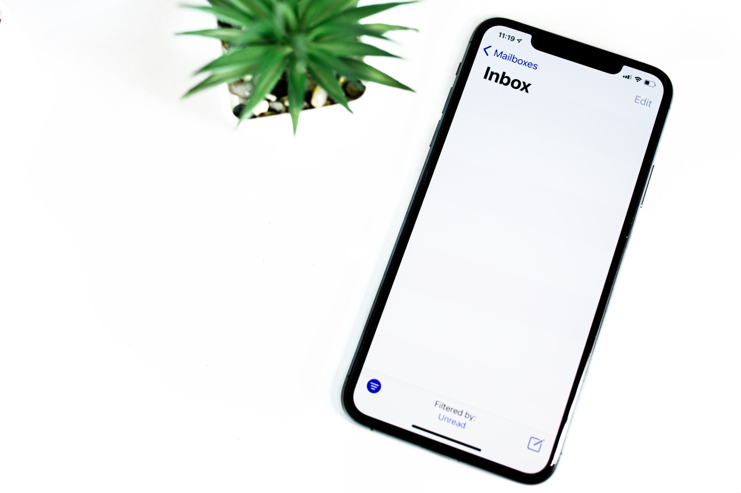 An iPhone next to a plant displaying an Outlook email on its screen.
