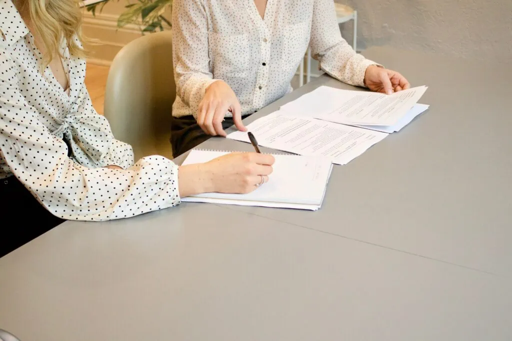 Two women sitting at a table signing agreement for IT consultation services.