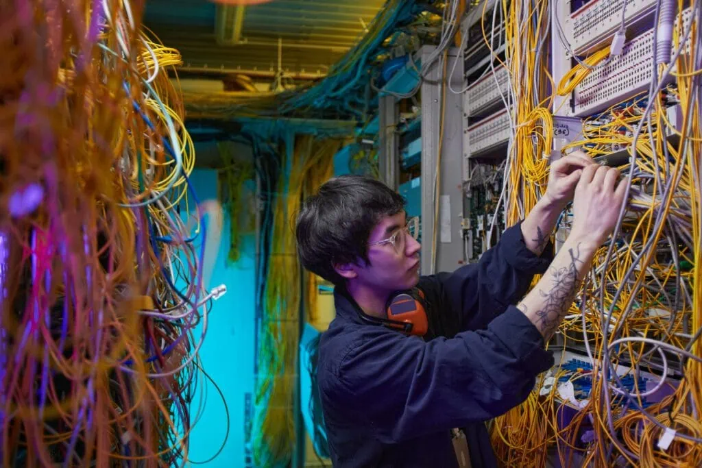 A man is working on a computer in a room full of IT network services.
