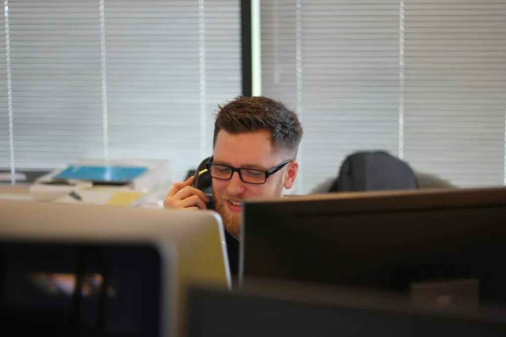 A man on desktop providing remote IT services while communicating with client on a phone.