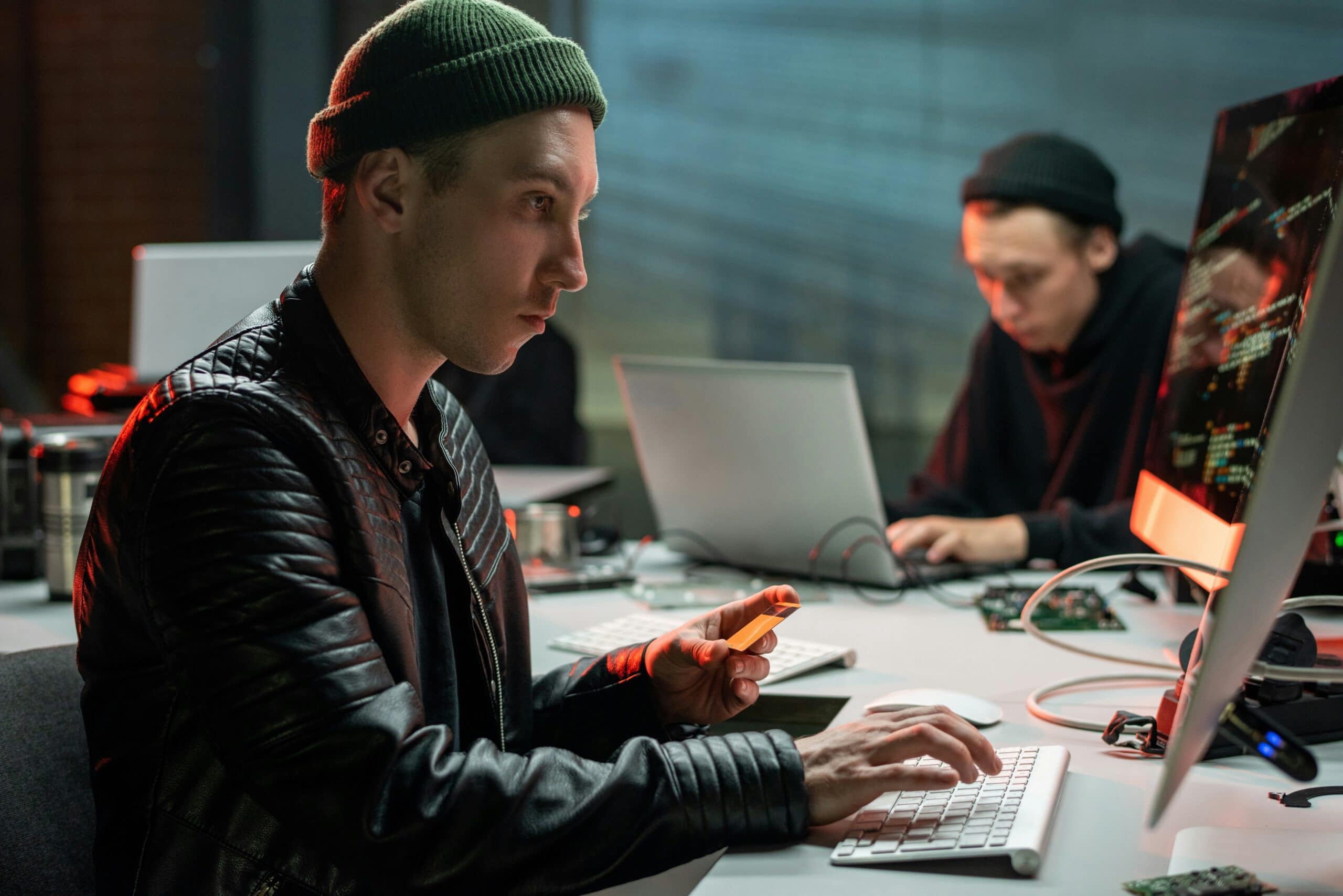 A man wearing a beanie is using a computer for cyber-attacks.