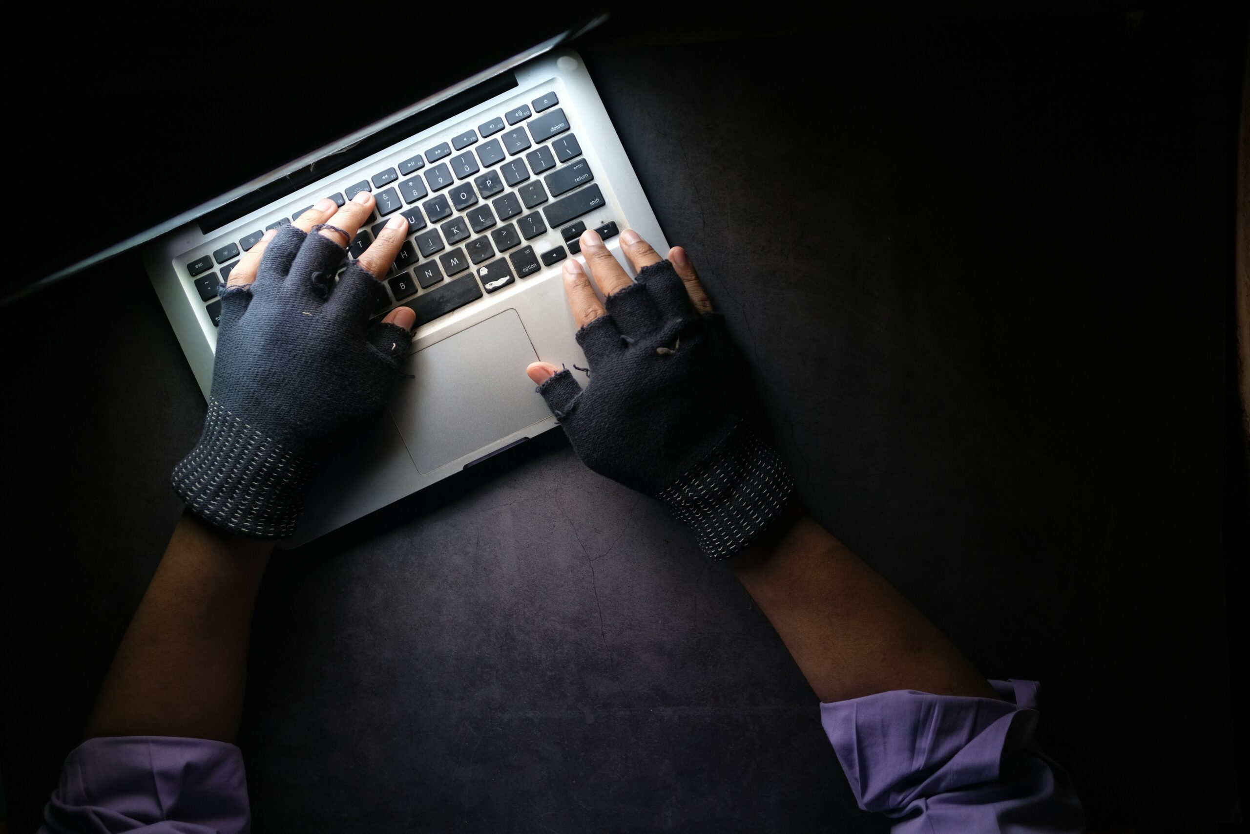 A person wearing gloves typing on a laptop in a mean and menacing manner, possibly engaged in a cyberattack.
