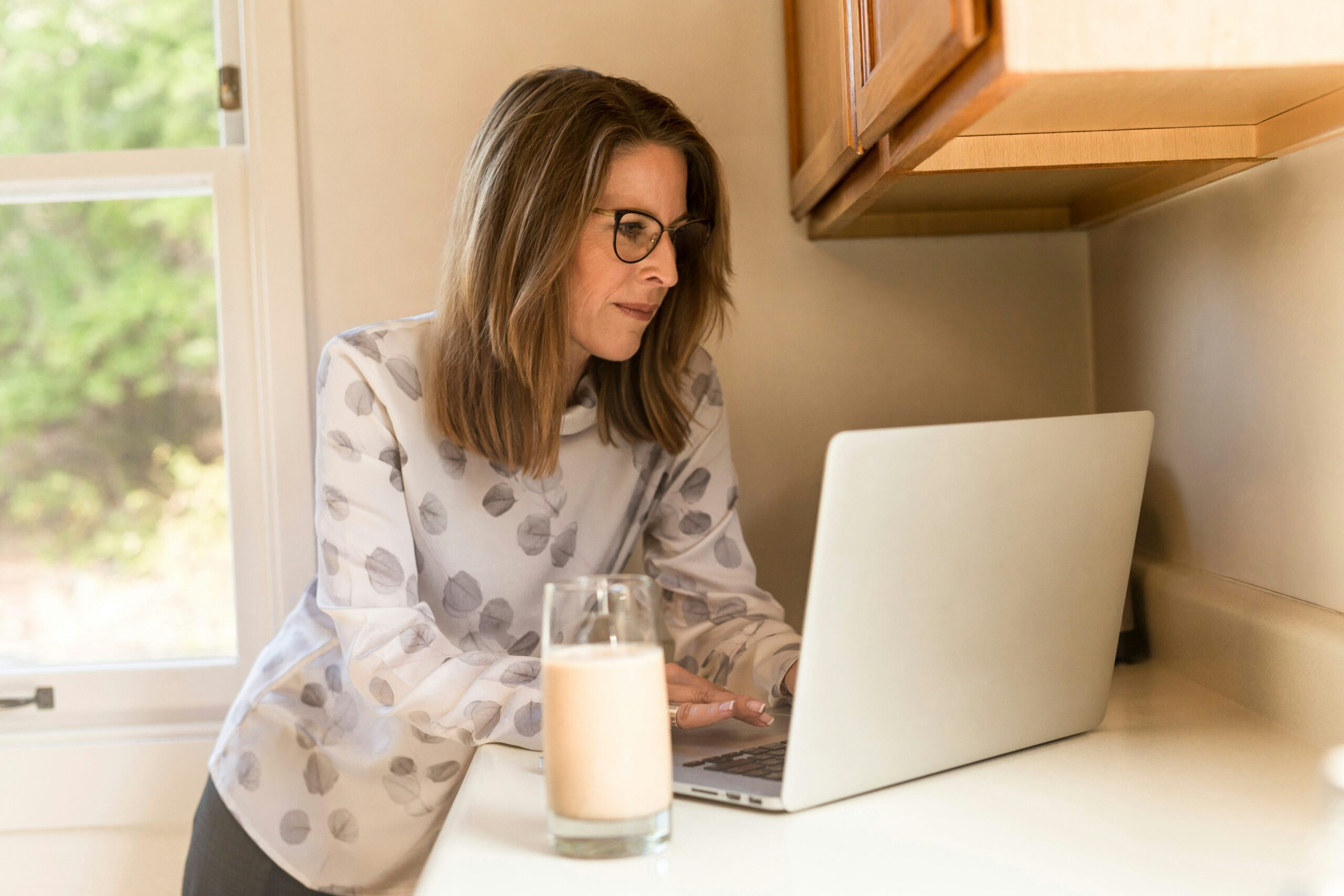 A woman enhancing her cybersecurity awareness in her kitchen while using a laptop to review small business sales.