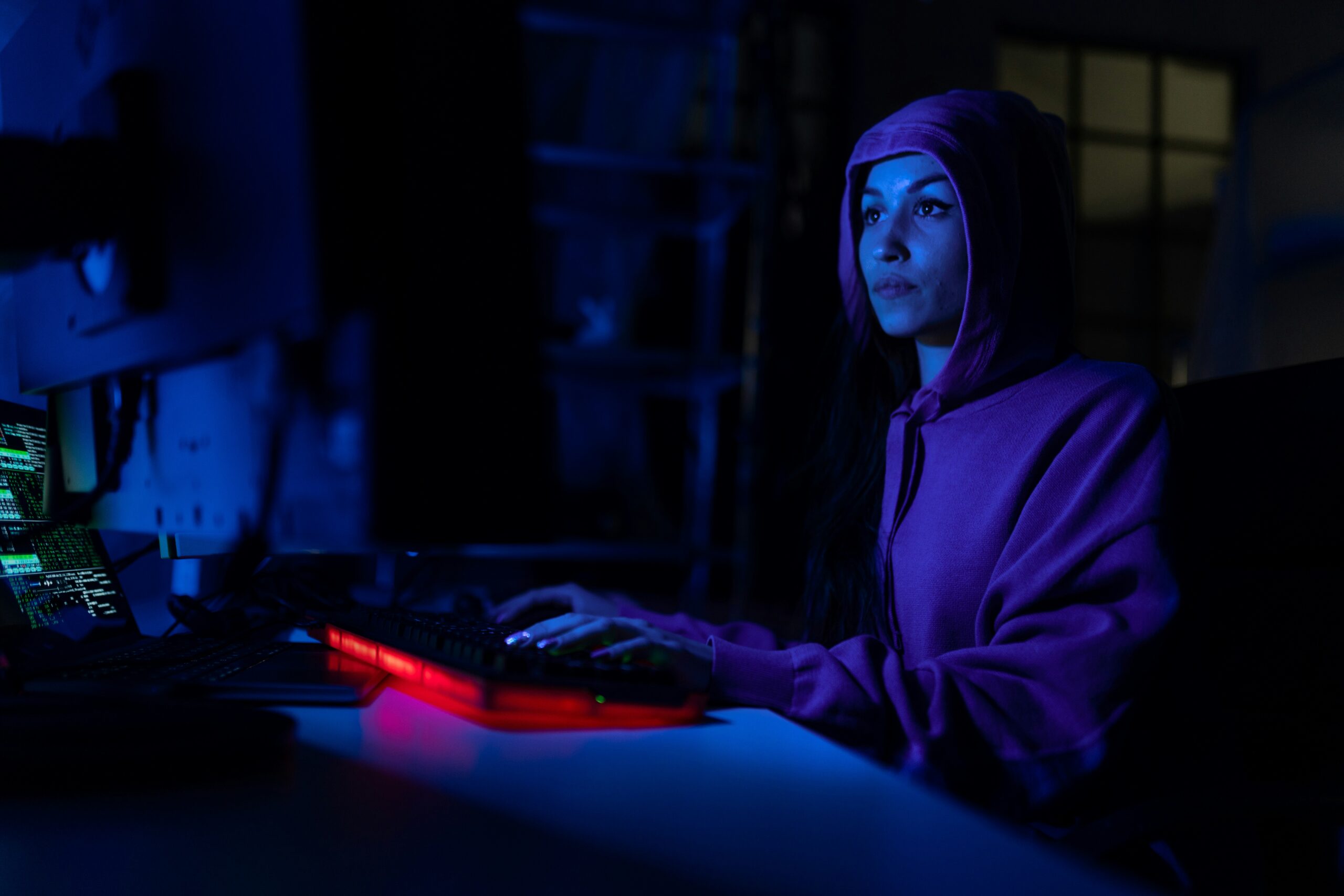 A woman in a purple hoodie sitting at a computer, researching 10 ways to protect your computer from hackers.
