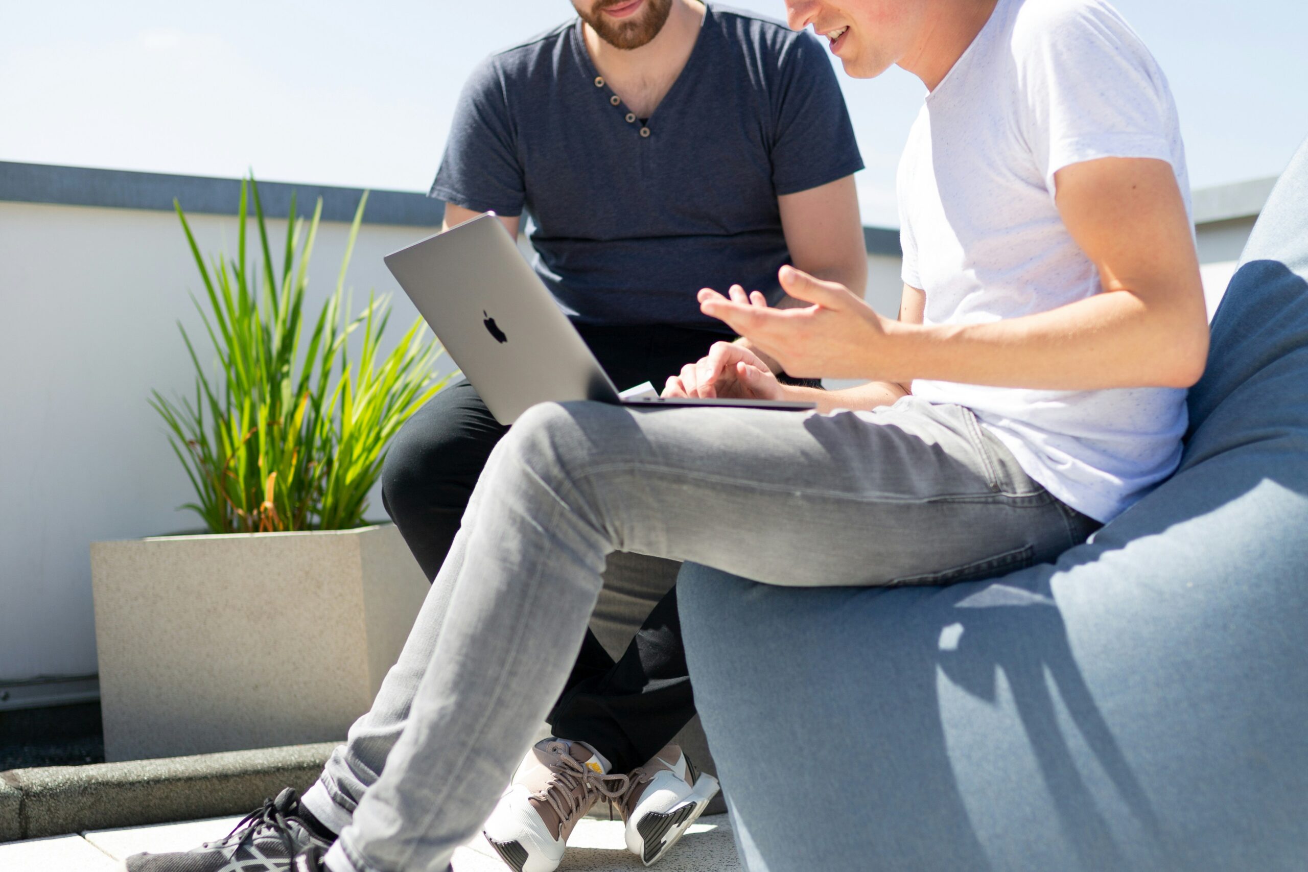 Two individuals in casual attire having a discussion about managed services benefits with a laptop outdoors.