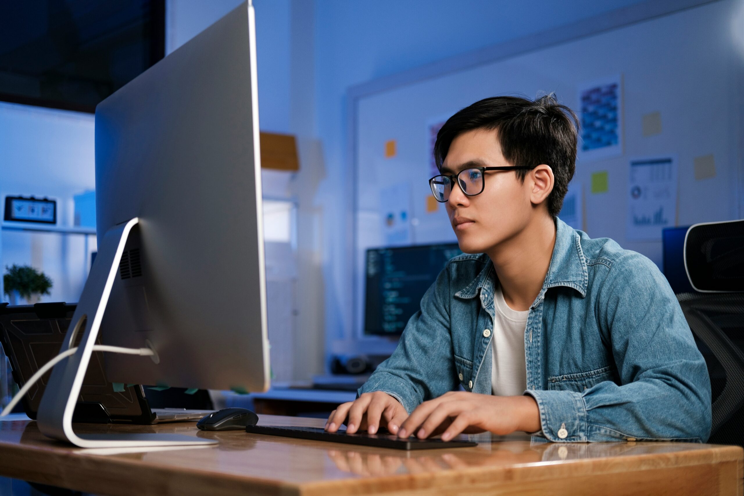 Young man concentrating on managed IT while working on a computer in a dimly lit office.