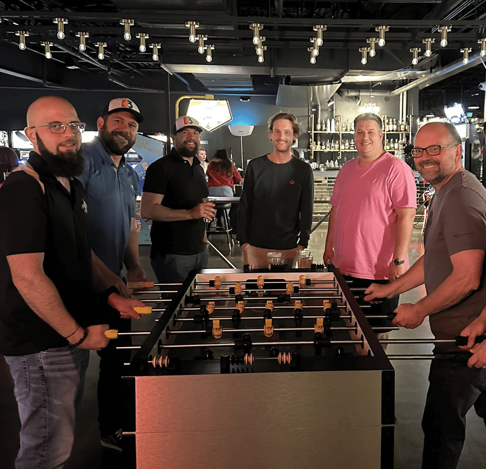 Group of people enjoying a game of foosball at a social venue with Why Choose K3.