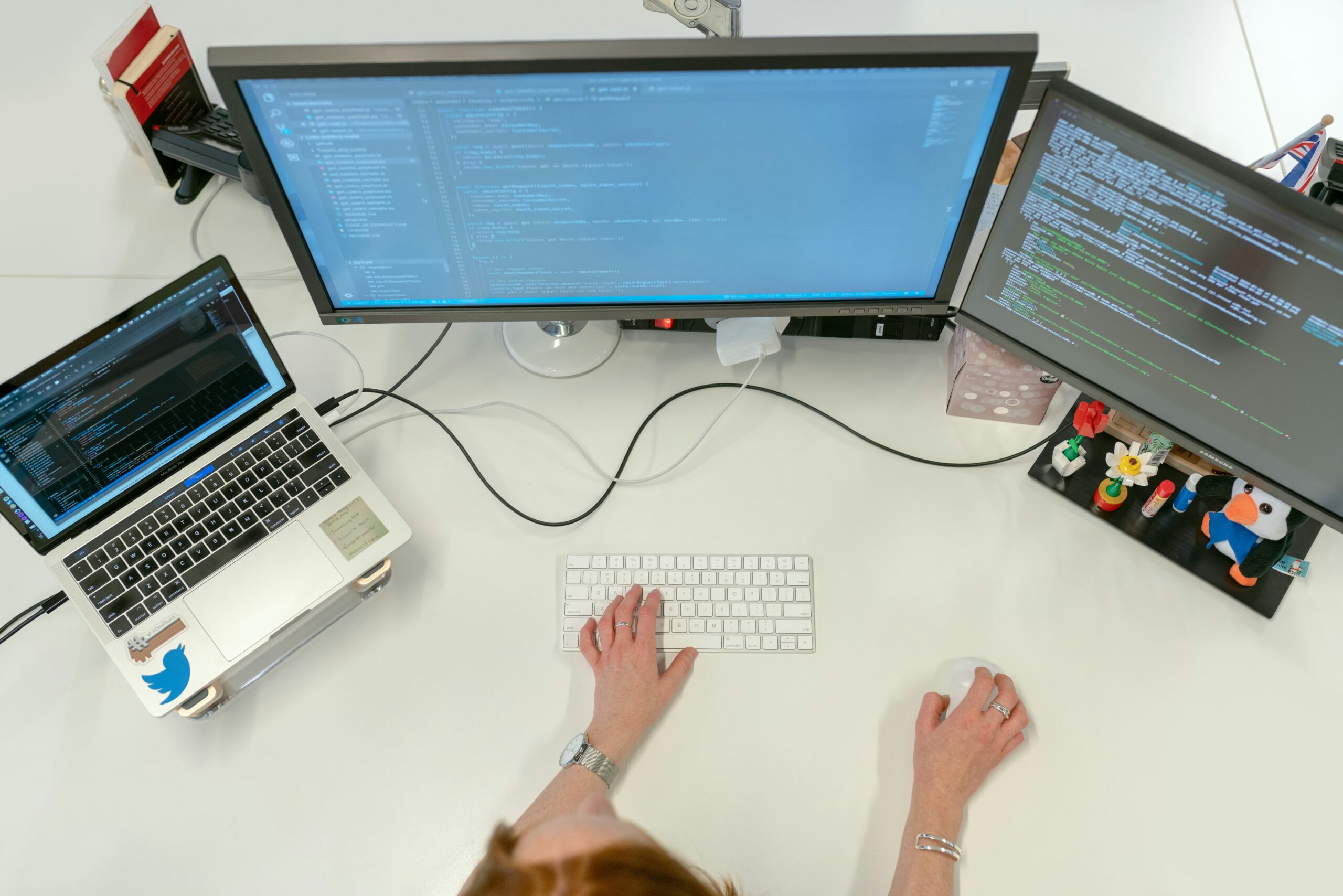 A person typing on a keyboard at a desk with three computer screens displaying code related to fully managed IT services and a laptop on the side.