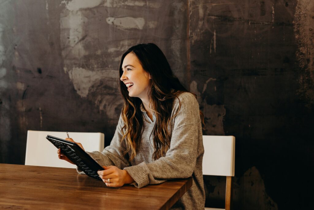 Smiling woman sitting at a wooden table with a clipboard after devices were fixed by provider of IT services for business.