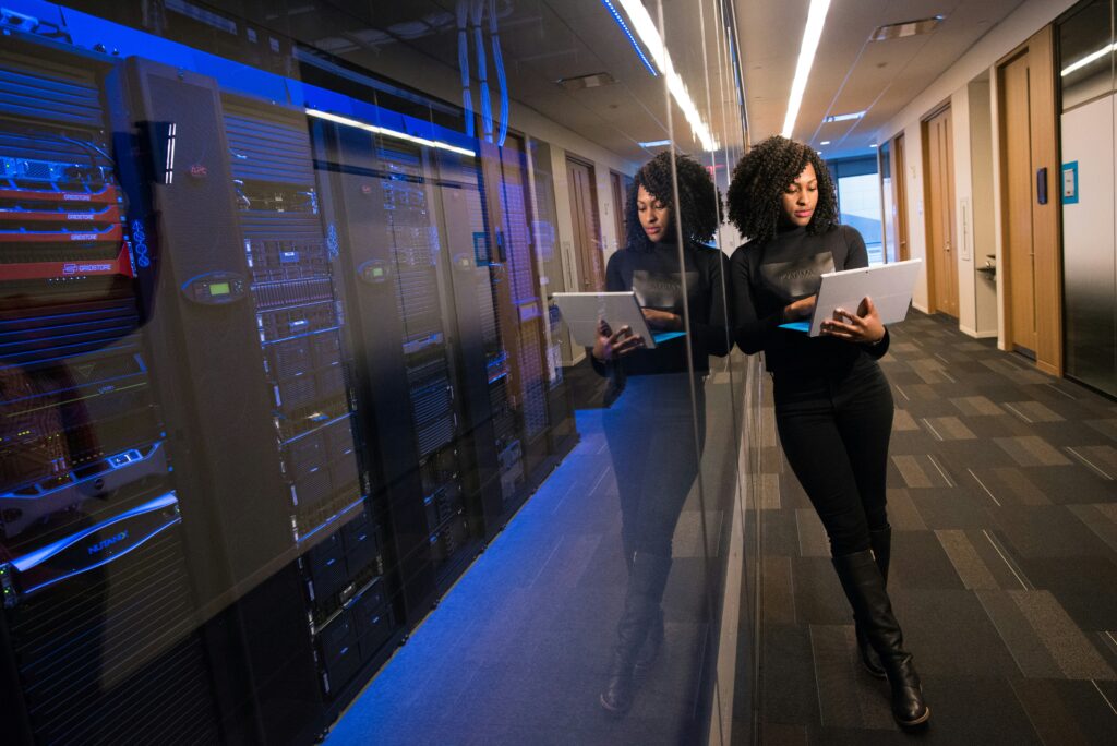 Professional analyzing data on tablets next to server racks in a managed technology services data center.