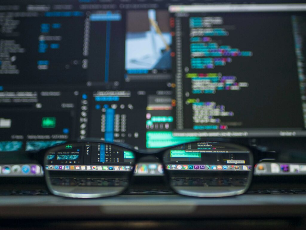 Eyeglasses in focus with blurred computer screens displaying code written for small businesses in the background.
