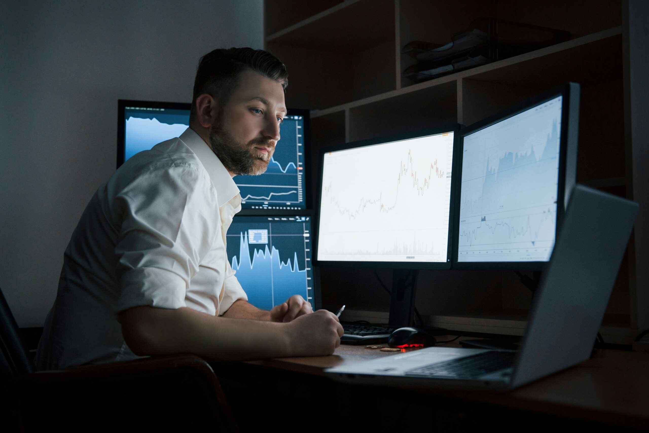 Man analyzing financial data on multiple computer screens in a dark room to understand what are managed services for SMB.