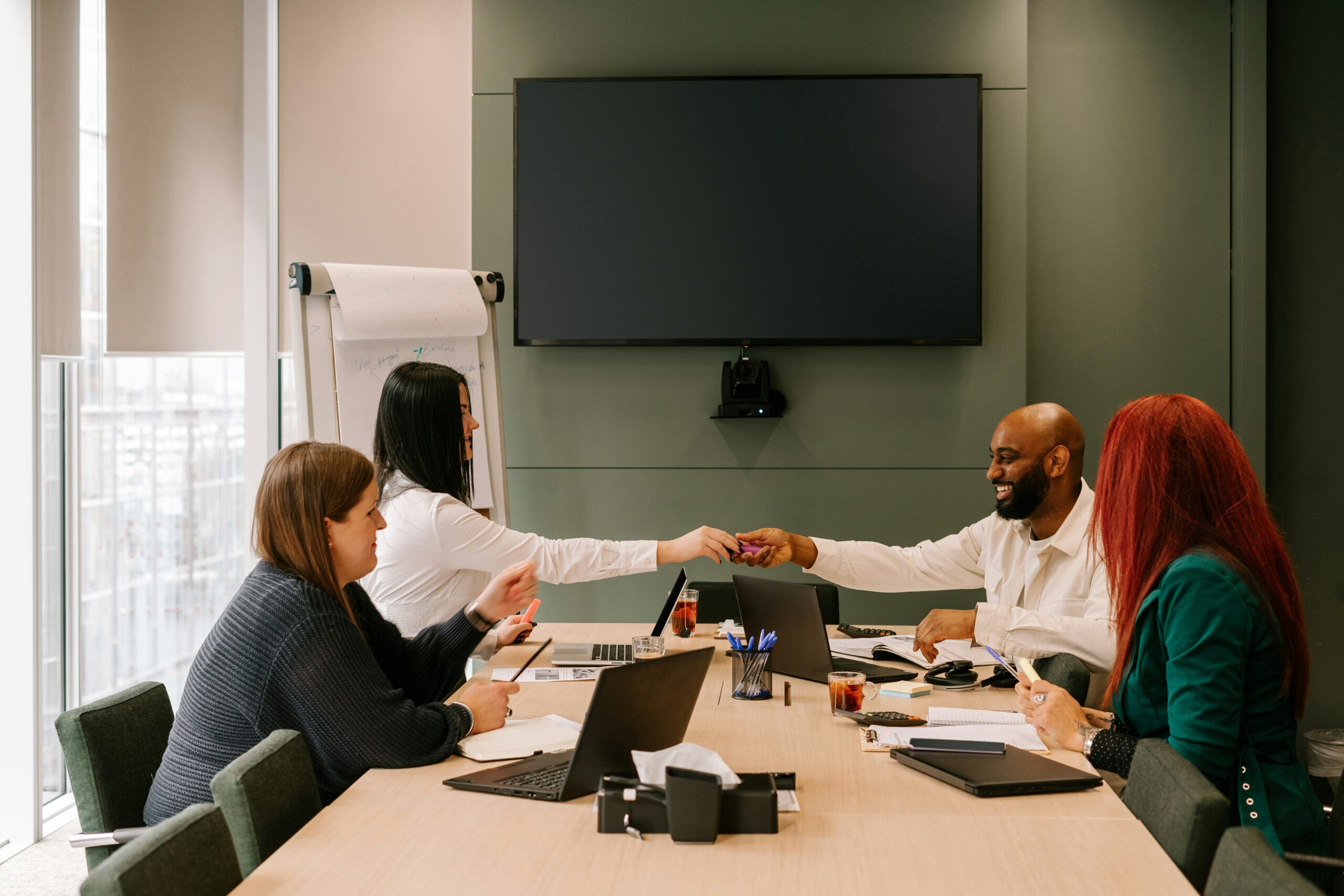Two colleagues shaking hands across a table in a meeting room, exemplifying what makes a good IT consultant, with other team members looking on.