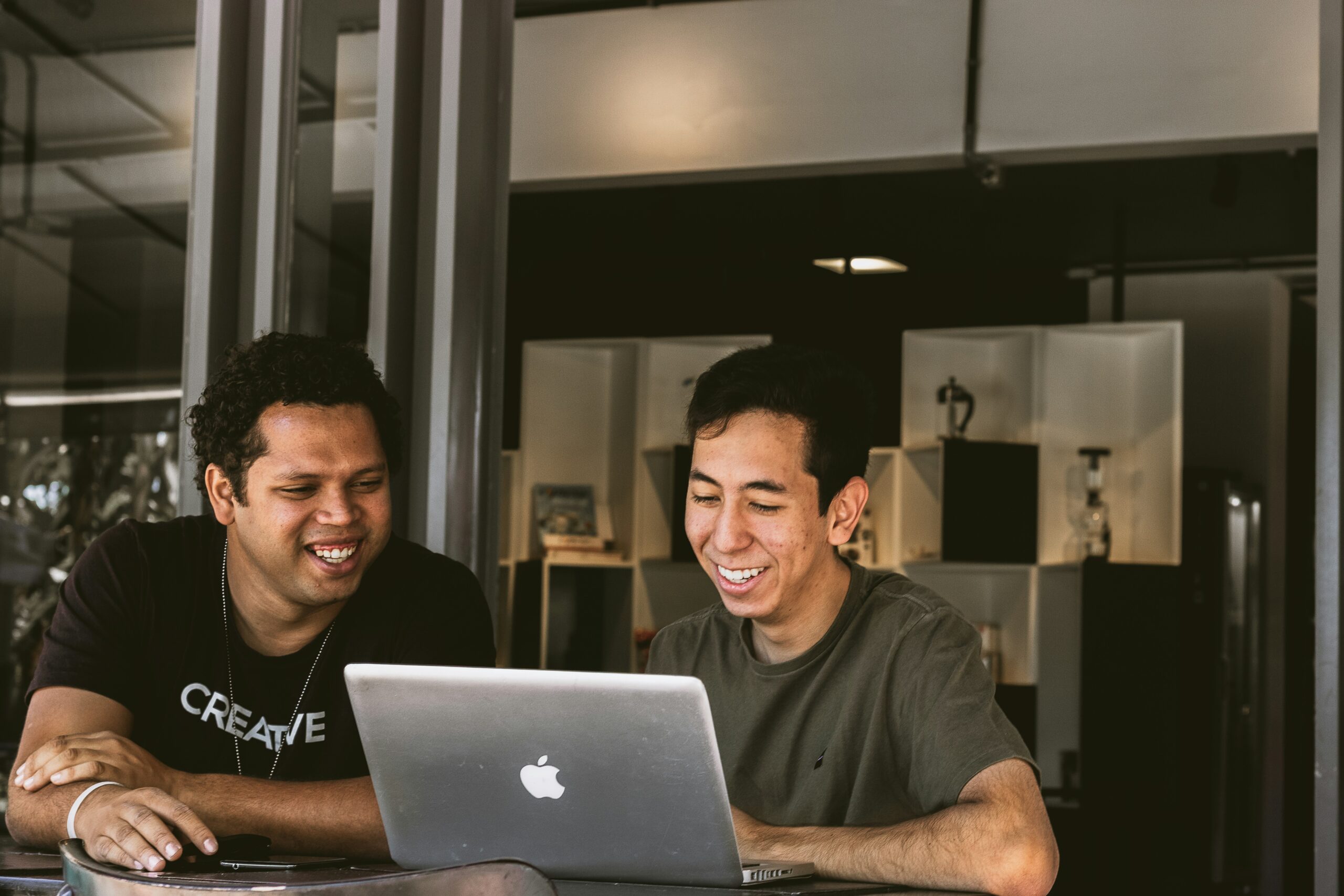 Two men laughing and looking at a laptop screen together, discussing IT service management principles and practices in a modern office setting.