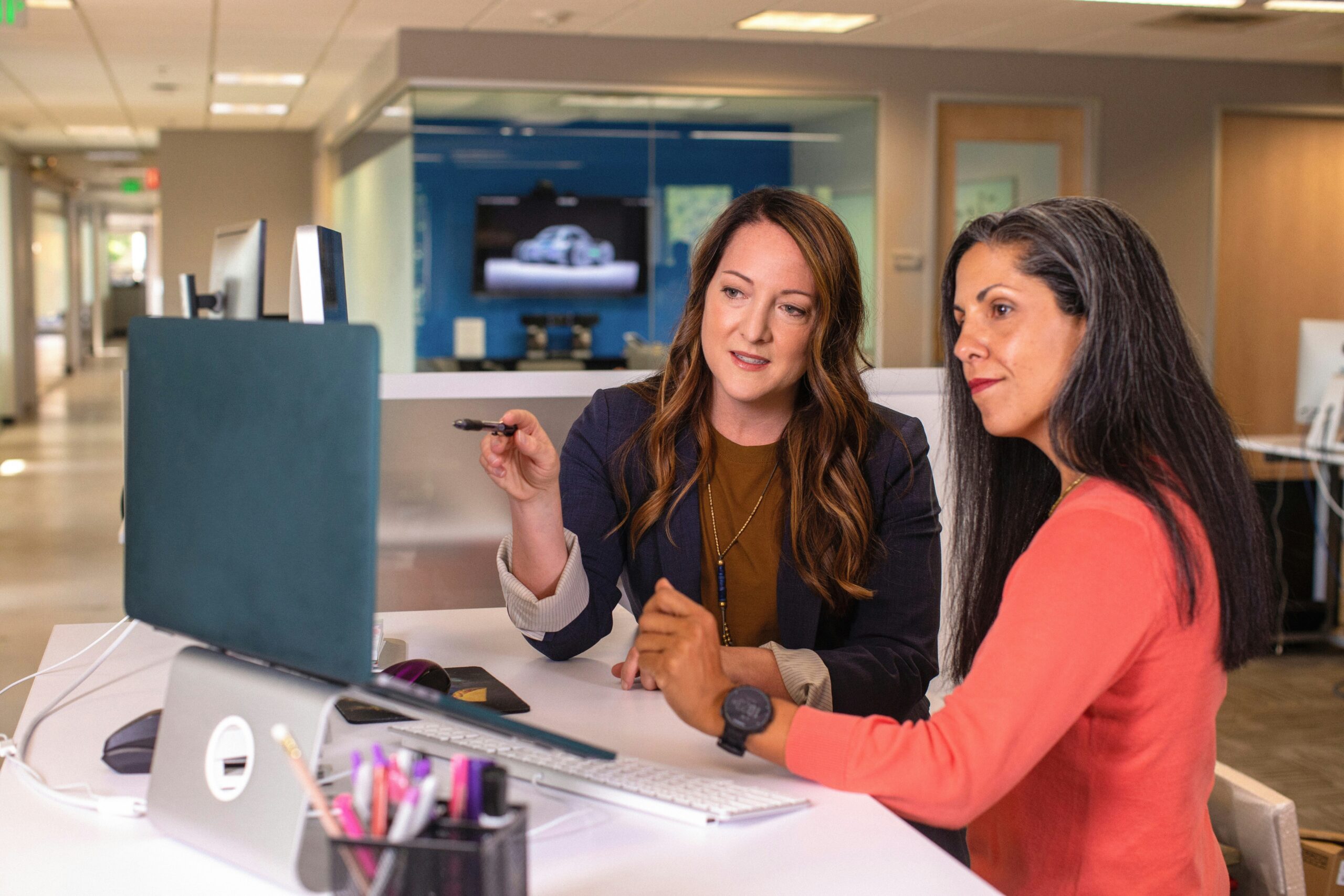 Two women review IT consulting content on a computer screen in a modern office, one pointing at the screen while discussing.