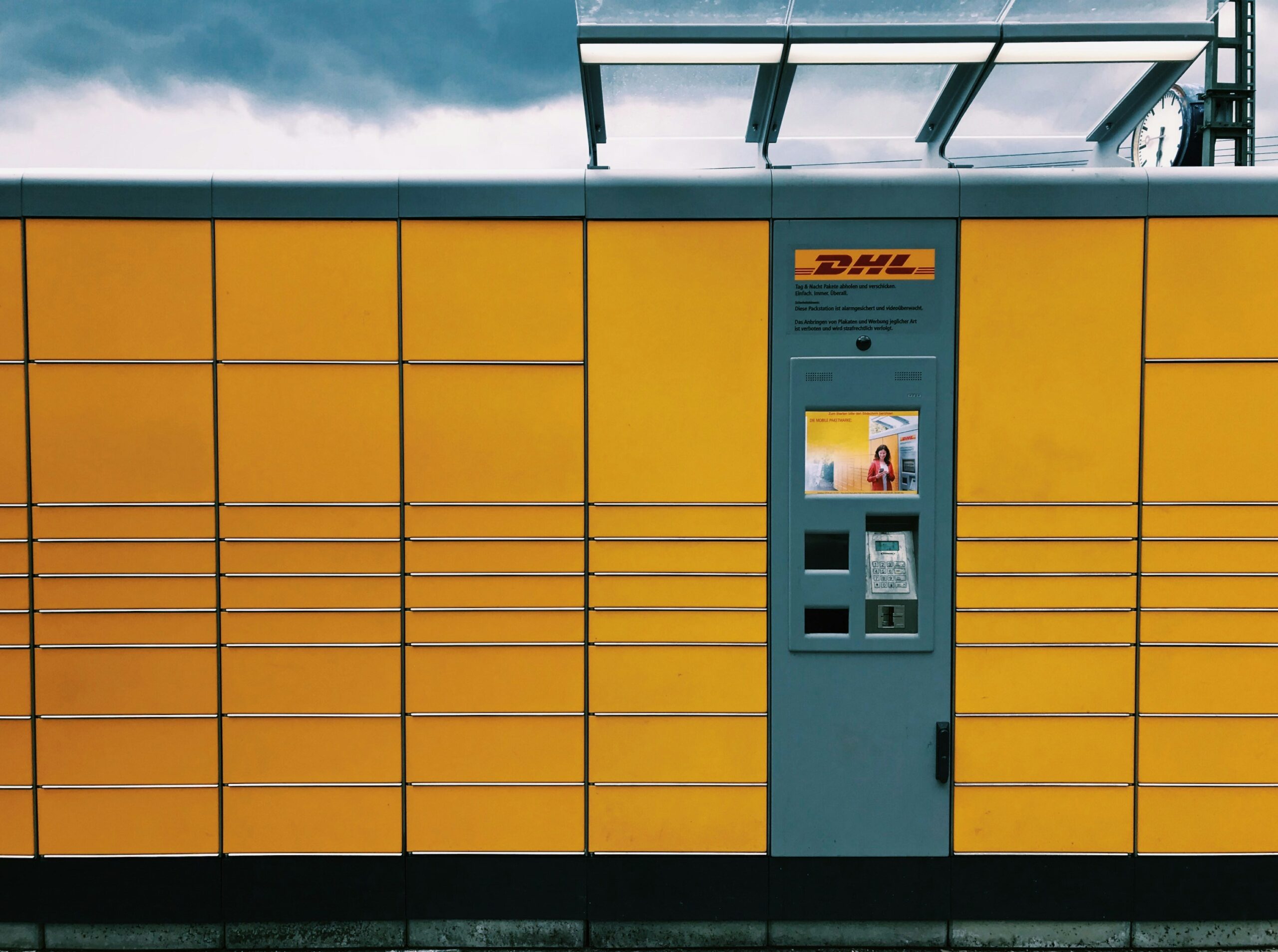 A DHL package locker system with yellow and gray compartments and a self-service kiosk, an example of process automation in logistics.