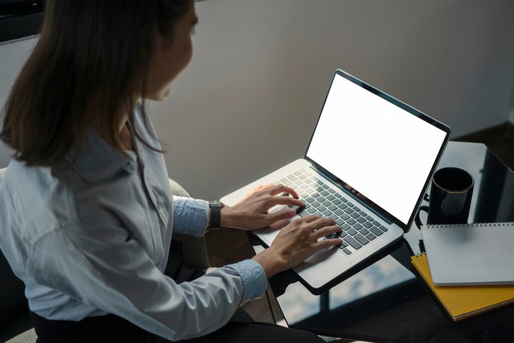 A person typing on a laptop with a blank screen, sitting at a table with a notebook, pen, and a coffee mug, explores business process automation software.
